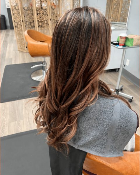 Mechas cobrizas sobre castaño con ondas al final, hechas en el salón
